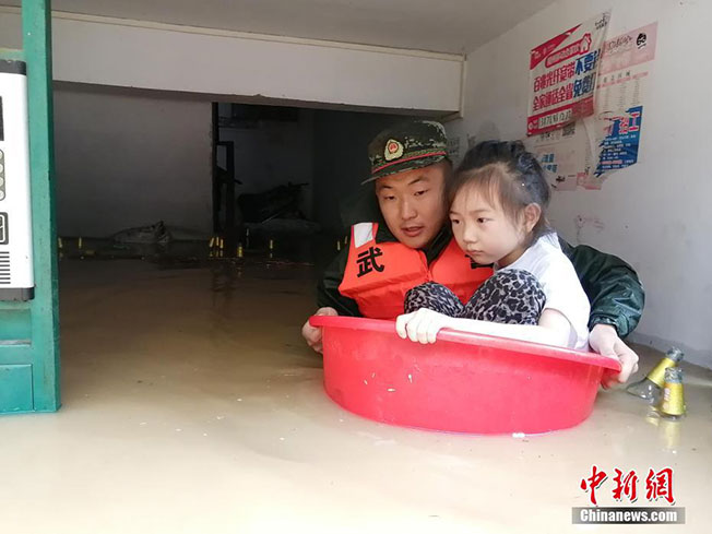 武警官兵把小女孩放在水盆中，带着她撤离灾区。（中新网）