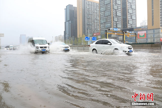 暴雨导致郑州街头周日积水，车辆涉水通行。（中新网）