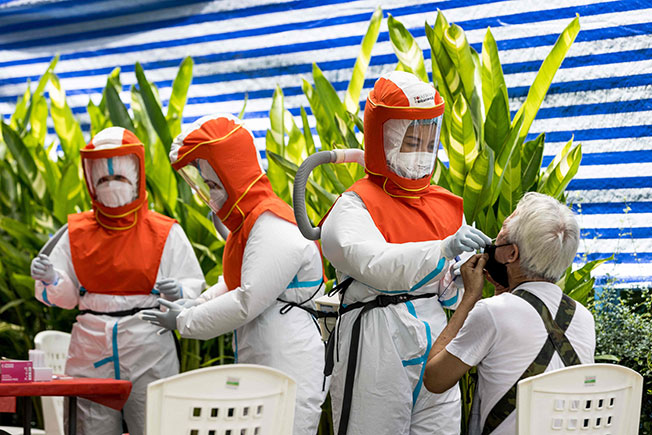 身穿个人防护设备的卫生员，周六在曼谷为民众展开检测。（法新社）