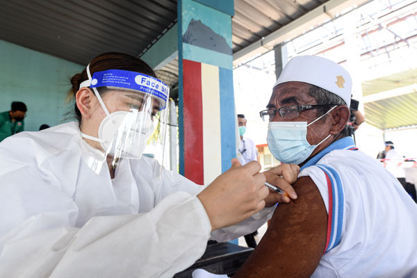一名医护人员（左）正在专注为拉拉本岛居民施打单剂康希诺疫苗。（马新社）