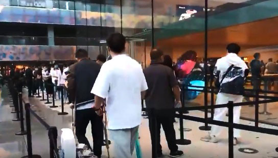 北京三里屯苹果商店一名男子虽然脚受伤柱着拐杖，却不减兴致想要排队购买iPhone 13手机。