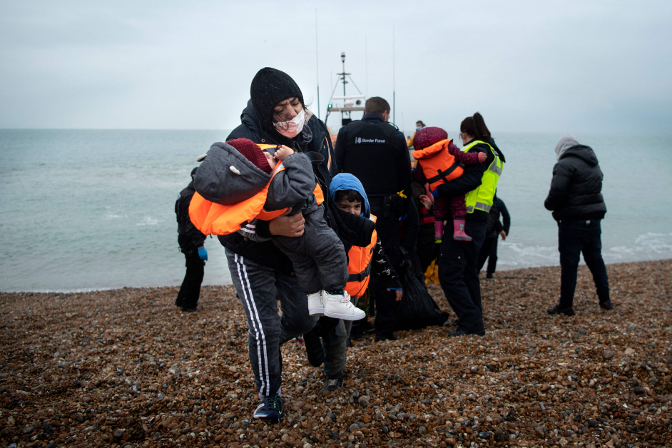 一名女移民边抱着年幼孩童，边牵着较大孩子走上海岸。 （法新社）