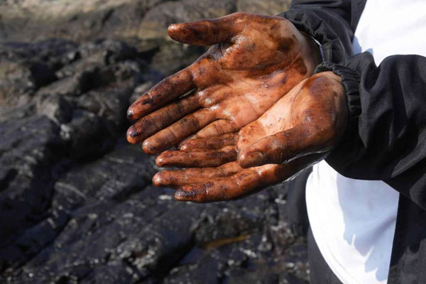 路人展示手上来自卡韦罗海滩的油污。