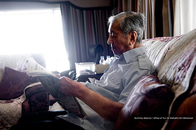 马哈迪坐在家中沙发上阅读报章，跟进时事发展。
