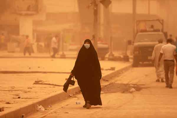 巴格达周一被泛出橘色光芒的浓密尘云笼罩，民众戴着口罩出行。（欧新社） 