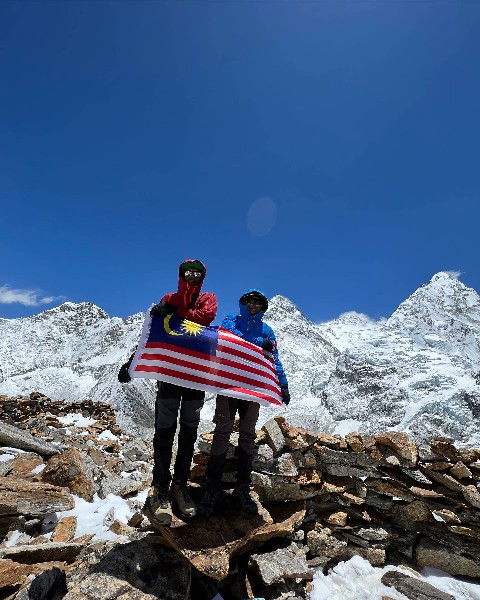 大马登山团队队员手持国旗，站在海拔5800公尺的普莫里高地营地拍照。