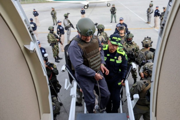 乌苏加在警员的押送下，登上飞机。