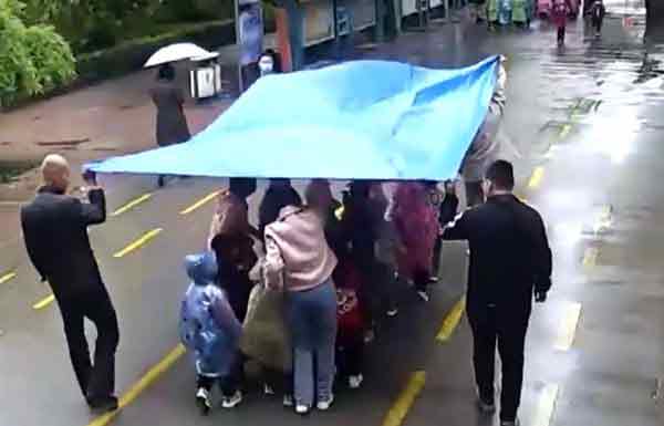 　8名教师用遮雨布帮幼儿园学生挡雨。