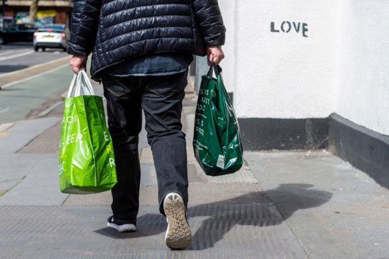 伦敦一名男子手提购物袋走在路上。（新华社)