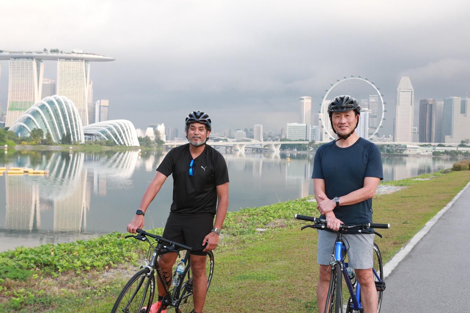 凯里（左起）和王乙康一同骑脚车，欣赏新加坡湖边景色。