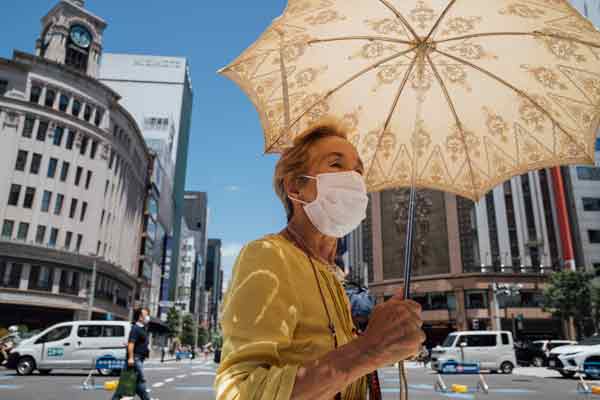 日本迎来高温天气，行人周日打着遮阳伞走过东京银座街头。（新华社）