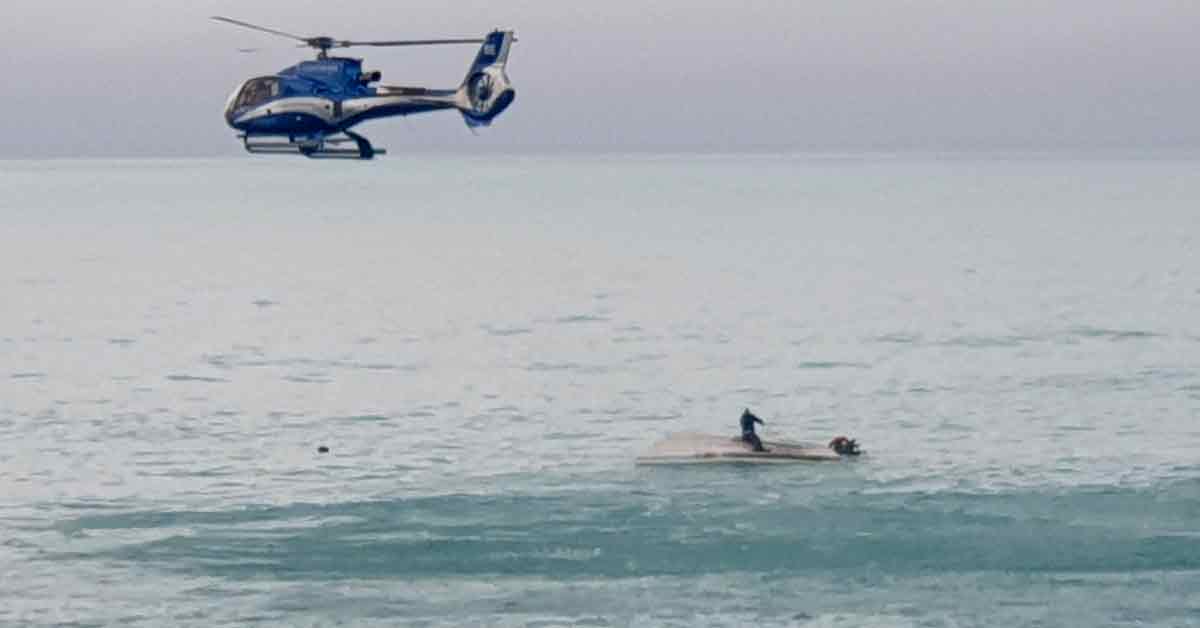 纽西兰赏鲸胜地凯库拉镇一艘船遭鲸鱼撞翻，一人坐在船肚上等待救援，当局出动直升机协助。（美联社）