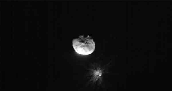 图为小行星“迪莫弗斯”及大哥“迪迪莫斯”，“迪莫弗斯”周边出现被撞击后的烟尘。
