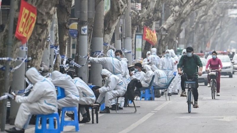 今年3月，上海防疫人员坐在封锁民宅大楼下歇息。