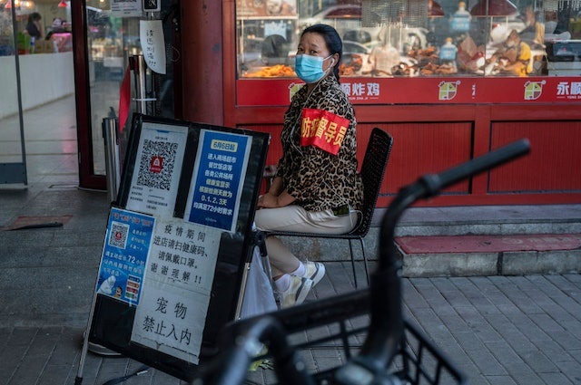 随着防疫进入新阶段，基层防疫手法备受争议。图为北京一名社区志愿者坐在健康码旁边。