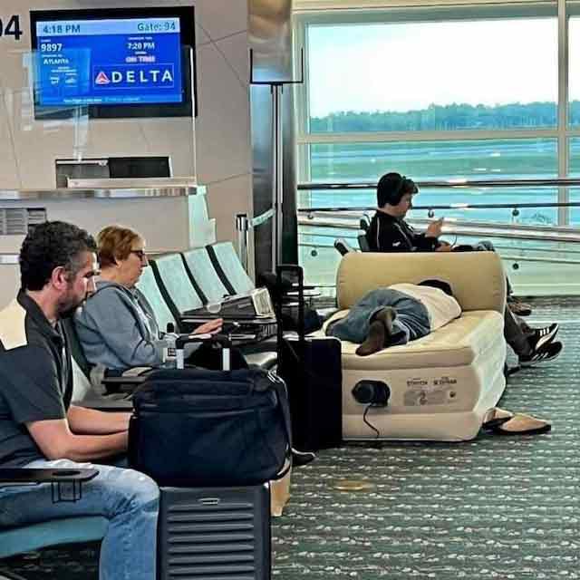 男子从自行携带的随身行李内拿出充气床垫，并睡在候机室中。