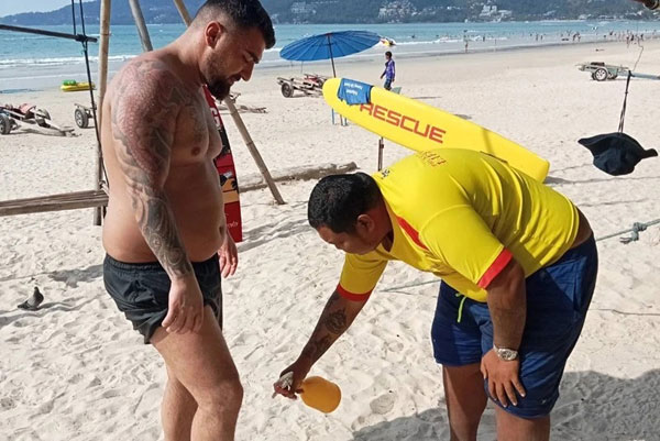 一名游客脚部被毒水母蜇伤，海滩救援员向他的伤口处喷洒药物缓解疼痛。