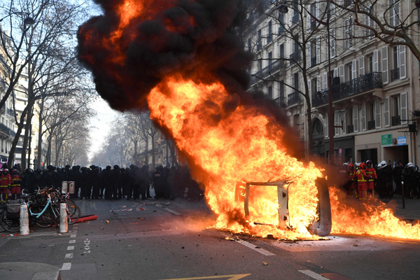 巴黎周六示威中，有车辆燃烧，车后方的是大批镇暴警察。（法新社）