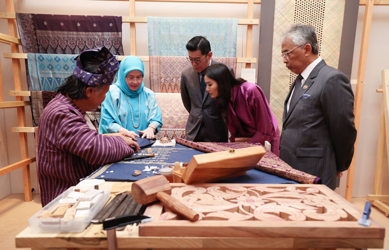 东姑阿兹札（左2起）向不丹国王伉俪介尚金锦缎的编织法，苏丹阿都拉（右）也细心聆听。