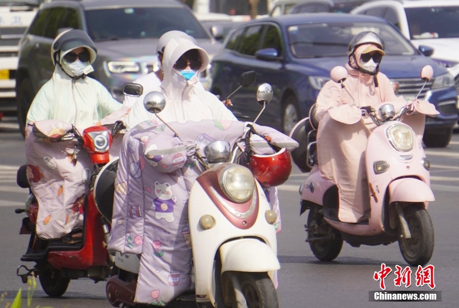 河南省郑州市周一迎来高温天气，市民“捂装”出行，穿戴防晒服、遮阳帽等防晒装备。（中新网）