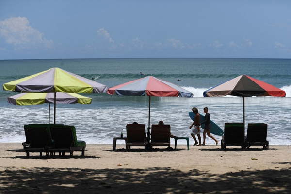 峇厘岛登巴萨附近的库塔海滩上，冲浪者拿着冲浪板在海滩步行。（法新社）