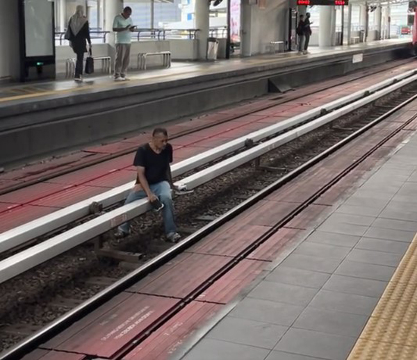 列车离开后，男子便瘫坐在铁轨的铁架上发呆。