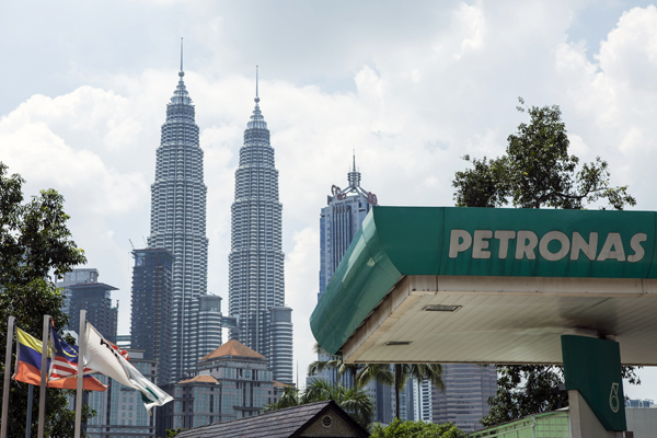 A Petroliam Nasional Bhd. (Petronas) gas station stands in front of the Petronas Twin Towers, second right, in Kuala Lumpur, Malaysia, on Friday, Feb. 27, 2015. Petronas, the Malaysian state oil company preparing for a leadership transition in April, reported a loss in the fourth quarter following crude's plunge. Photographer: Charles Pertwee/Bloomberg