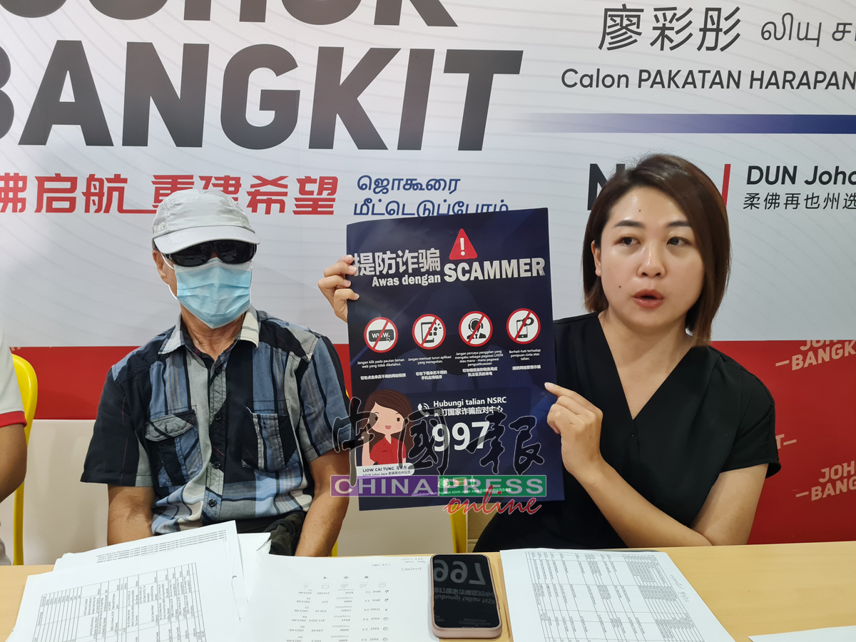 廖彩彤（右）出示自己办公室印制的反诈骗宣传，呼吁公众们提防诈骗，左为彭先生。