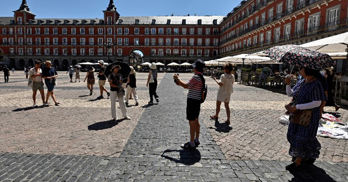 西班牙天氣酷熱， 遊客在馬德裏的馬約爾廣場參觀時紛紛撐傘遮陽。