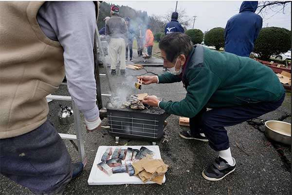 日本石川县珠洲市灾民在户外烤鱼。