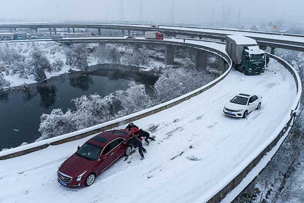 运遇上大雪，不少车困在了湖北武汉的高速公路上，包括汽油车和电动车。图为周二司机和乘客合力，把汽车从堆满雪的高架桥上向前推行。（法新社）
