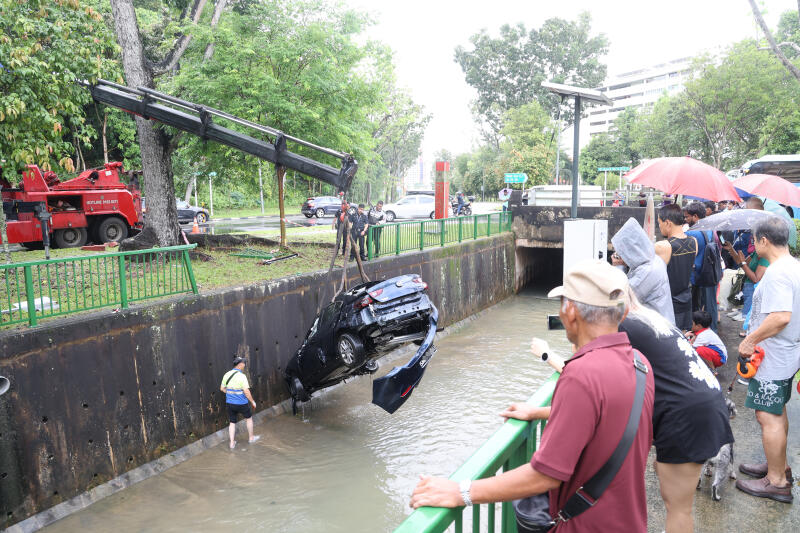 拖车公司出动一辆起重机吊起轿车，多名公众驻足围观。