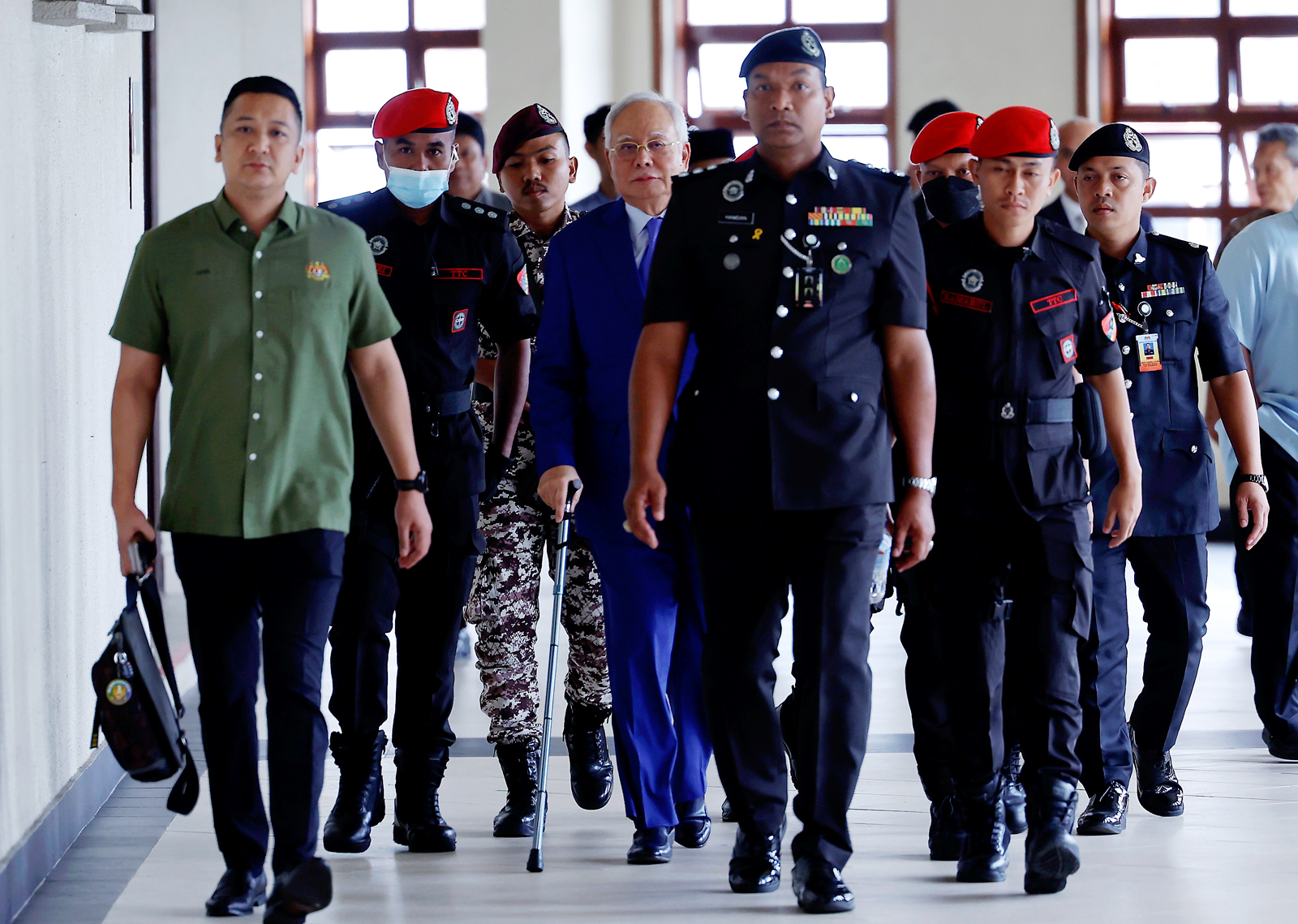 身穿西装的纳吉(中)身穿西装,继续拄拐杖出庭自辩。