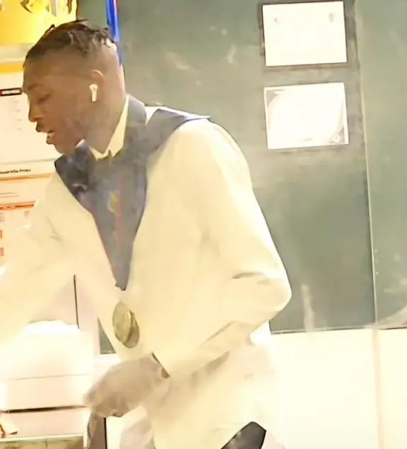 贝克工作时仍穿着毕业披肩和奖牌，戴上塑料手套为顾客打包订单。