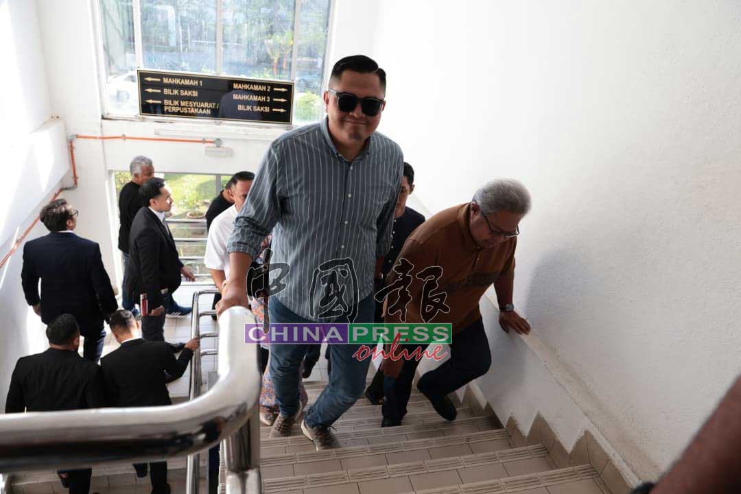 眼戴墨镜的阿克马（左）进入大山脚法庭时，显得轻松，对媒体面带微笑。